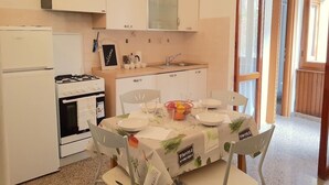 A compact kitchen with a refrigerator, stove, and sink. There is a table set for dining with chairs, and a chalkboard sign on the wall. - Augusto charming flat with sea view (Monterosso al Mare)