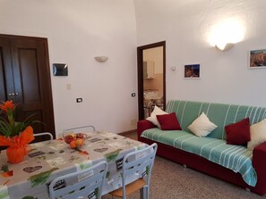 A small living area with a dining table, a green sofa, and a mirror.