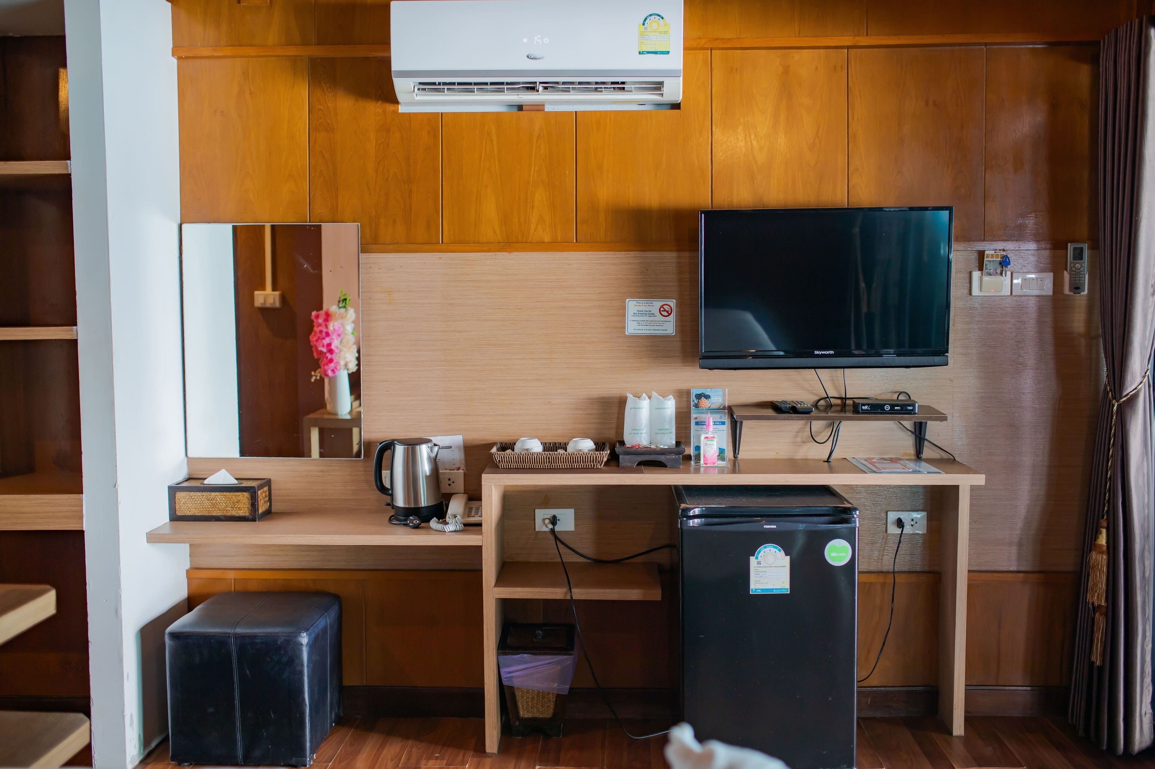 Una kitchenette compacta equipada con refrigerador, cafetera, hervidor de agua y televisor de pantalla plana montado en la pared.