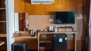 Una kitchenette compacta equipada con refrigerador, cafetera, hervidor de agua y televisor de pantalla plana montado en la pared.