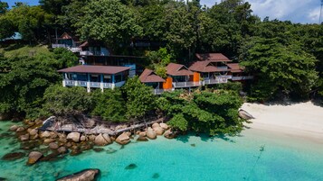 A coastal resort with multiple buildings surrounded by dense greenery and a clear turquoise beach.