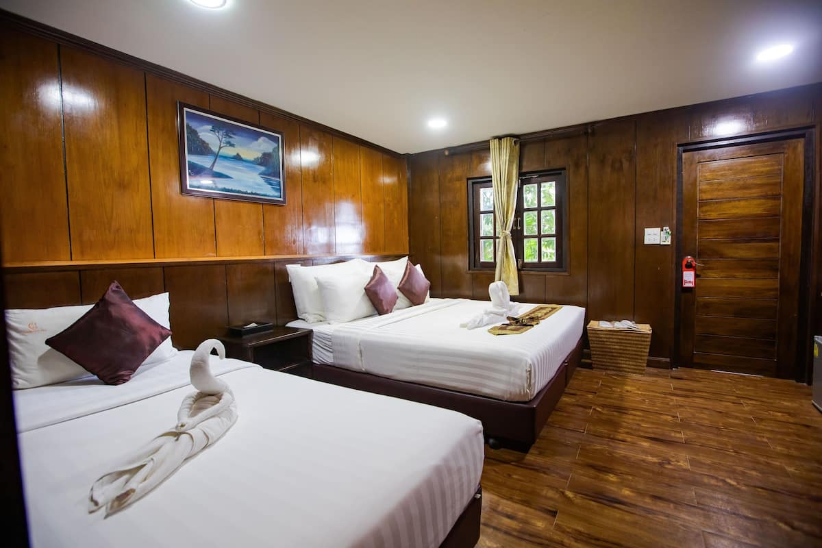 A hotel room with two beds, wooden paneling, a painting on the wall, and a window with curtains.