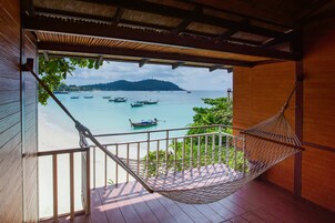 A hammock on a wooden deck overlooking a beach with boats and a distant island.