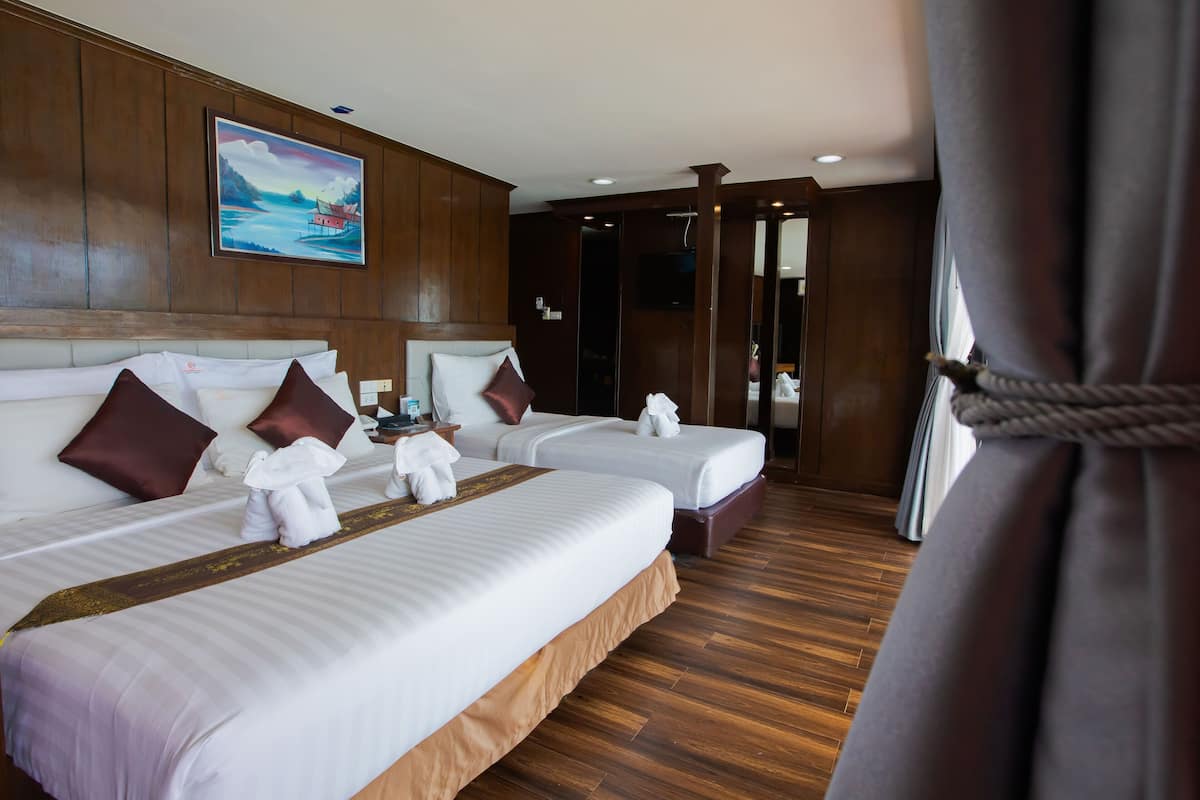A hotel room with two beds, wooden flooring, a painting on the wall, and a view of the sea through the window.