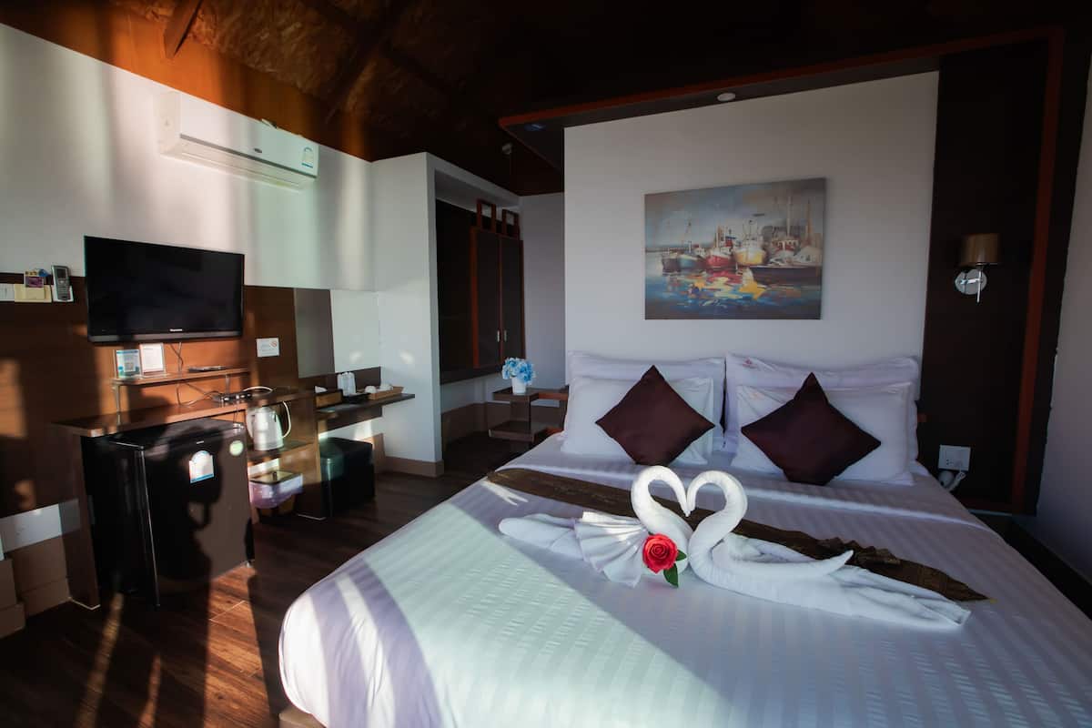 A hotel room with a bed, a TV, a desk, and a painting on the wall.