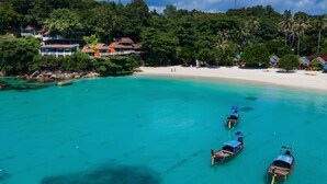 A coastal area with a sandy beach, several boats, and buildings surrounded by lush greenery. - Chareena Hill Resort - Pattaya Beach Koh Lipe (Koh Lipe)