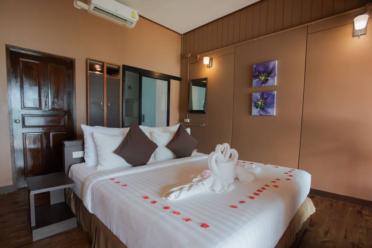 A hotel room with a large bed, a wooden wardrobe, a small table, and a wall-mounted air conditioner.