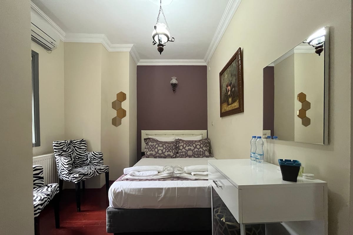 Habitación de hotel con cama, mesita de noche, silla, espejo y alfombra roja.