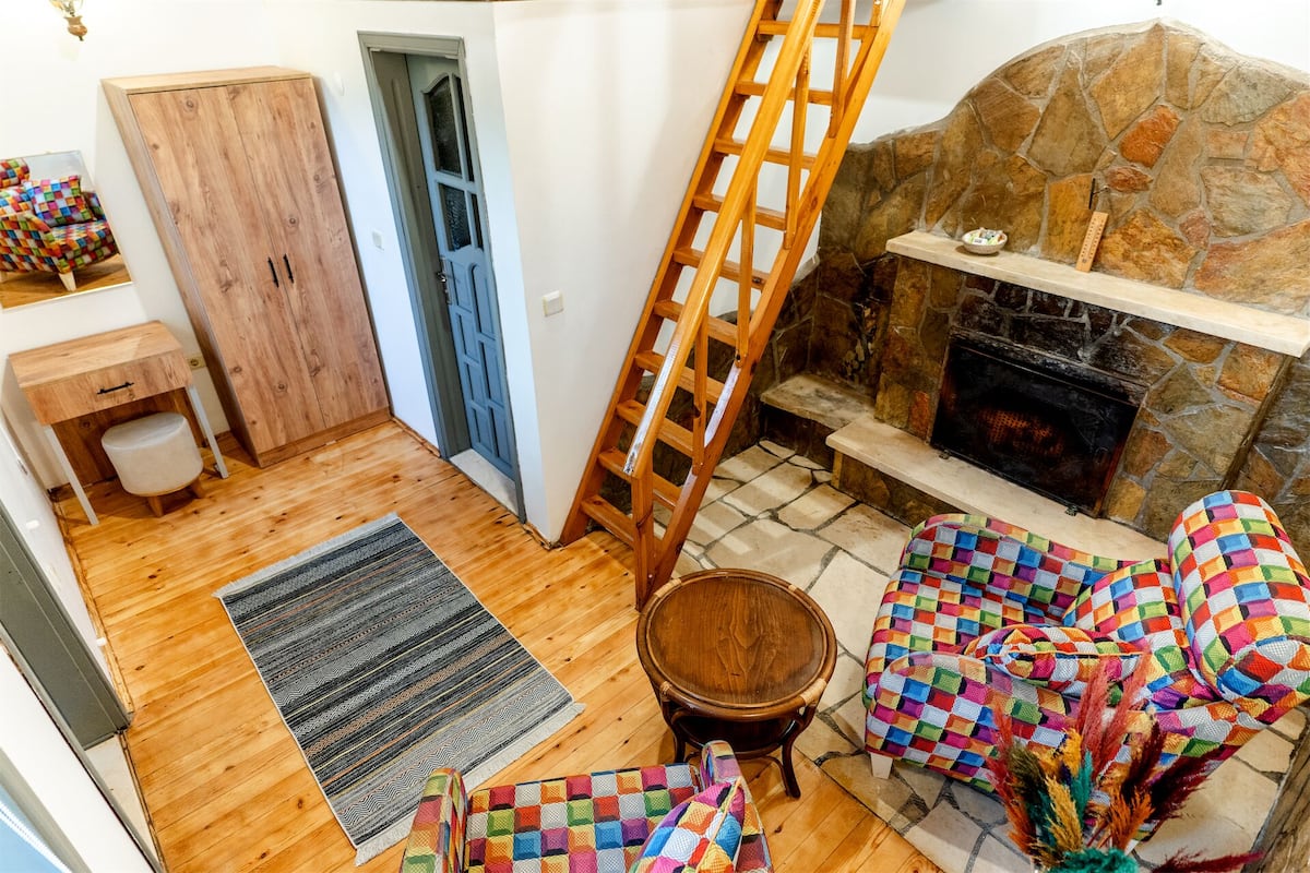 Una sala de estar acogedora con chimenea de piedra, una escalera de madera y muebles coloridos con diseños.
