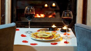 Una mesa con dos copas de vino, un plato de fruta y velas frente a una chimenea.