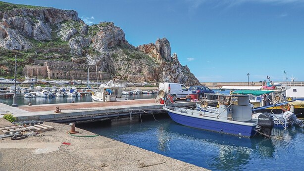 A marina with boats docked, a rocky cliff in the background, and a clear sky. - Amazing apartment in Buggerru with house sea view (Buggerru)