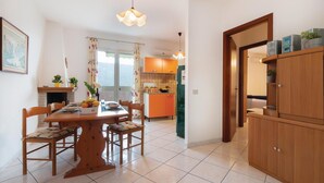 A dining area with a wooden table and chairs, a kitchen with orange cabinets, and a hallway leading to another room. - Amazing apartment in Buggerru with house sea view (Buggerru)
