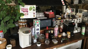 Una encimera de cocina desordenada con varios objetos, incluyendo una cocedora de arroz, botellas y un microondas.