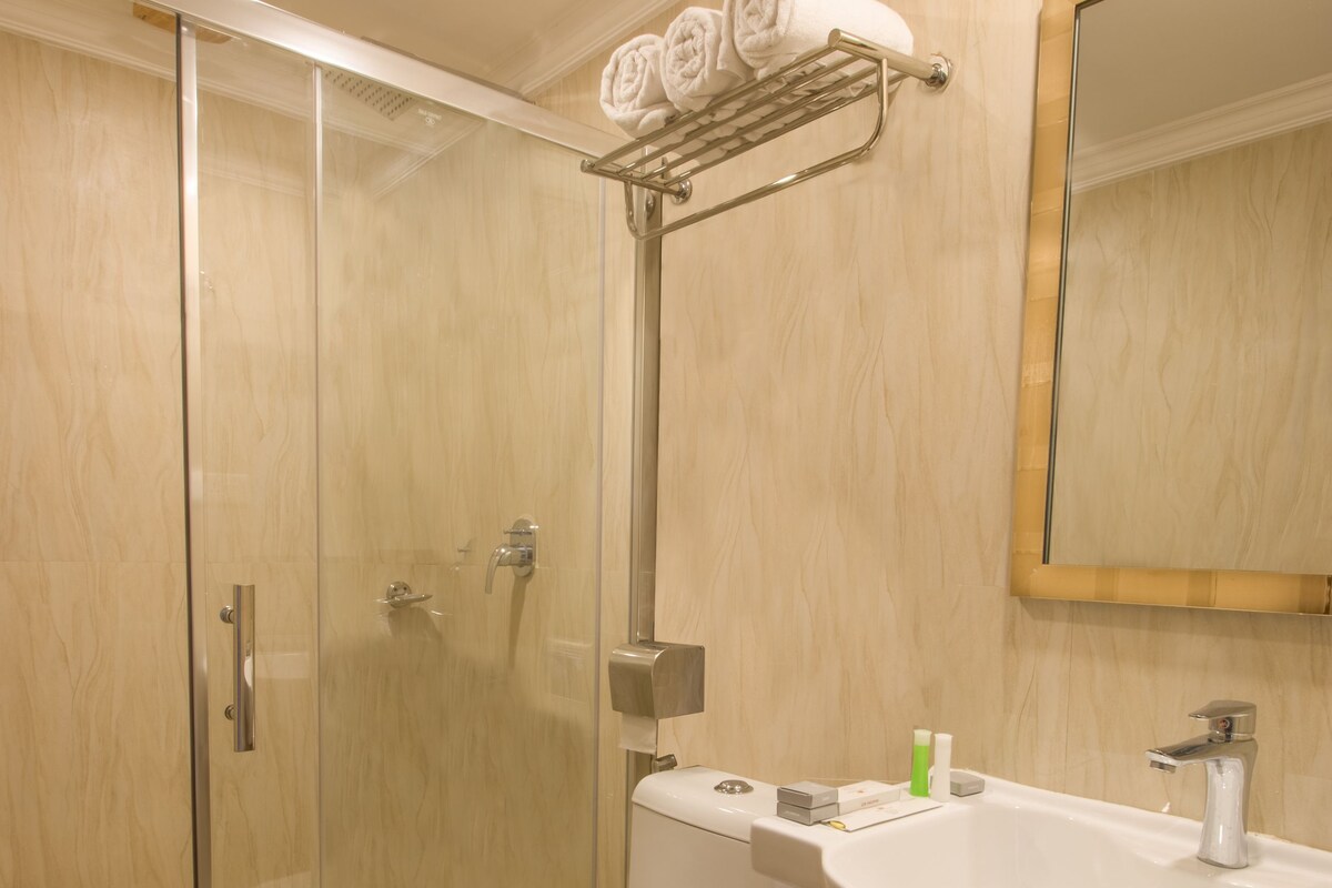 A bathroom with a glass shower enclosure, a toilet, a sink, and a towel rack with towels.
