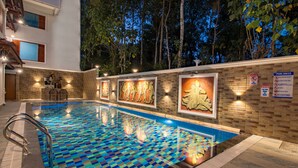 Una piscina con un diseño de baldosas a cuadros, rodeada por un muro de ladrillo con cuadros enmarcados y un letrero con las normas de la piscina.