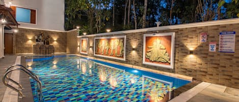 Une piscine dont le fond est recouvert de carreaux disposés en motif à damier, entourée d’un mur de briques orné de tableaux encadrés et d’un panneau indiquant les règles d’utilisation de la piscine.