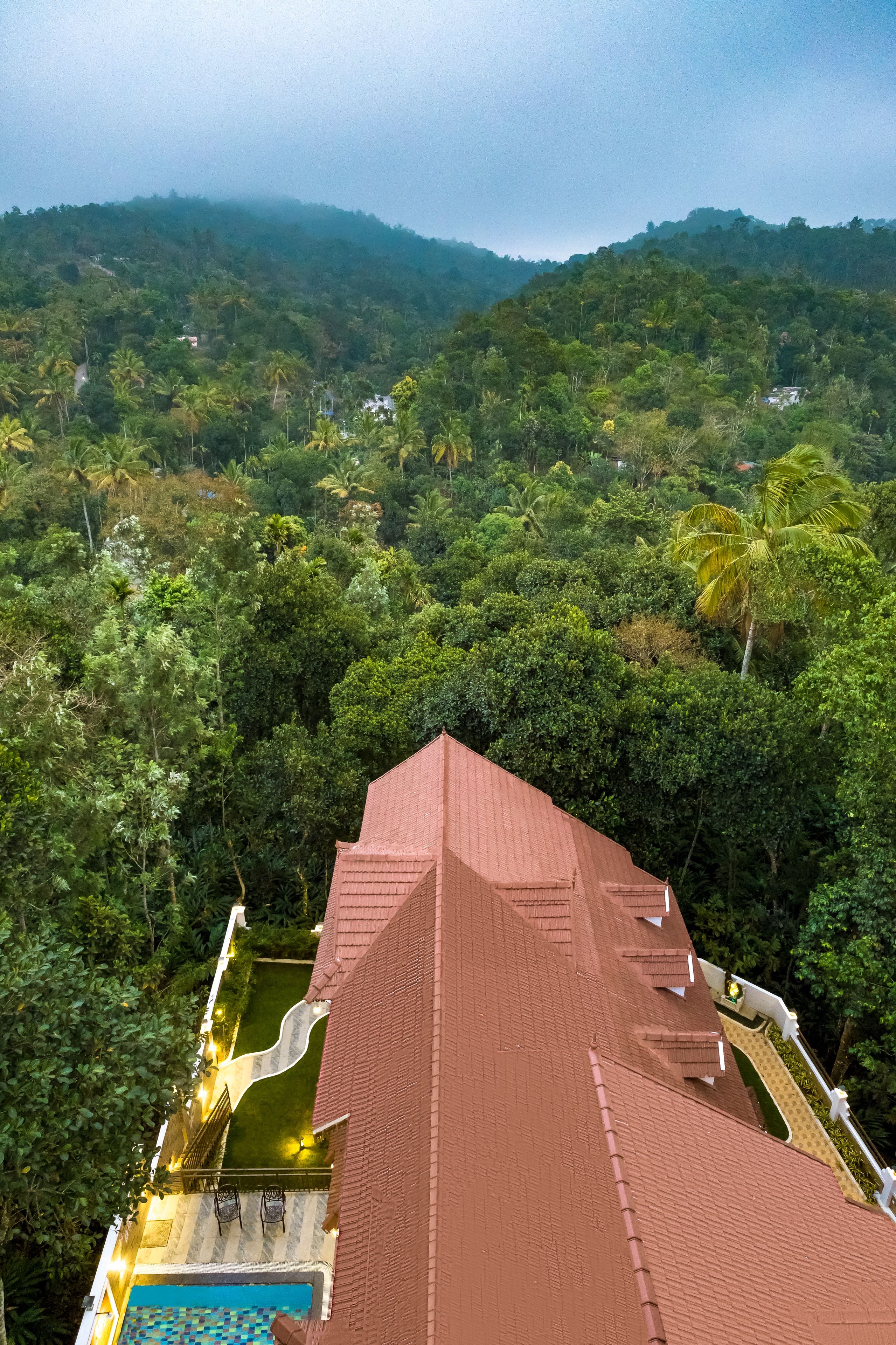 A hotel with a red roof, a swimming pool, and lush greenery in the background.