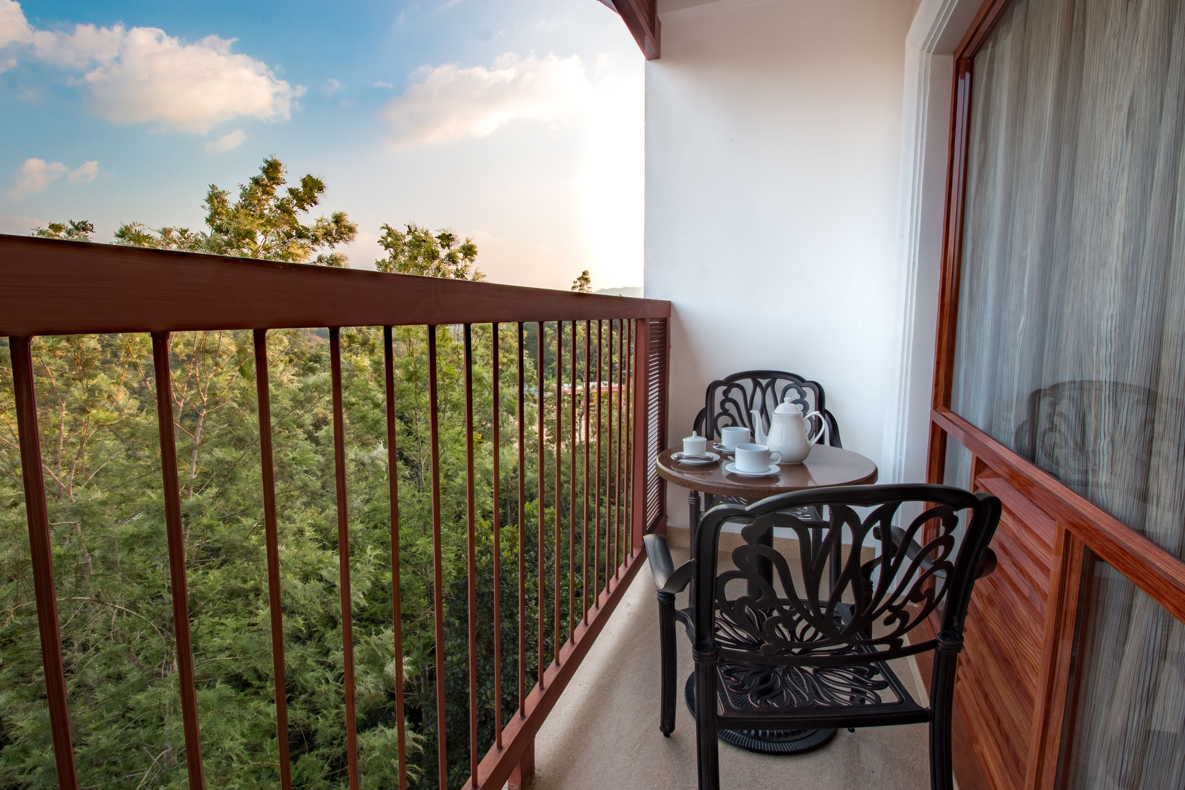 Ein Balkon mit Blick auf dichtes Grün, ein Tisch mit Teekanne und Tassen sowie ein Stuhl.