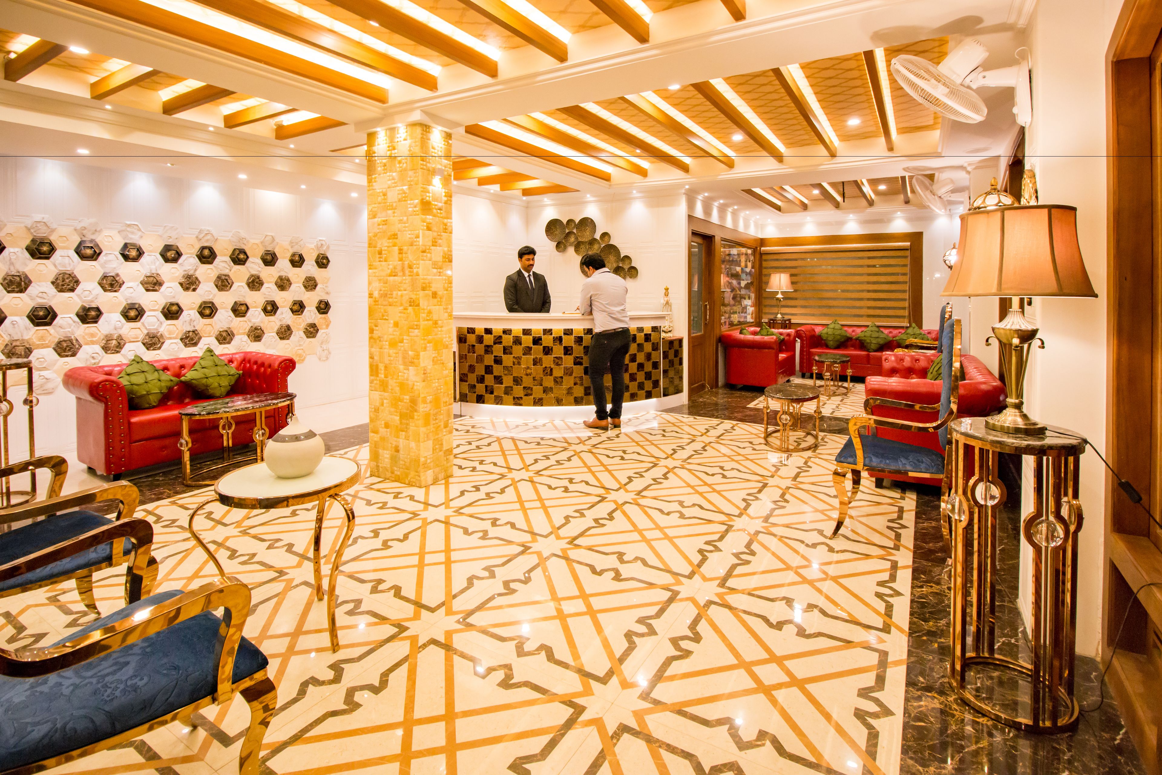 Um hall de hotel com balcão de check-in, sofás vermelhos, piso estampado e mesa de recepção.