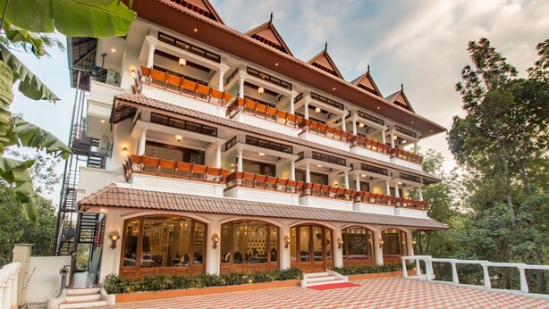 A multi-story building with a traditional architectural style, featuring balconies and large windows. - Crown Valley Thekkady (Peermade)