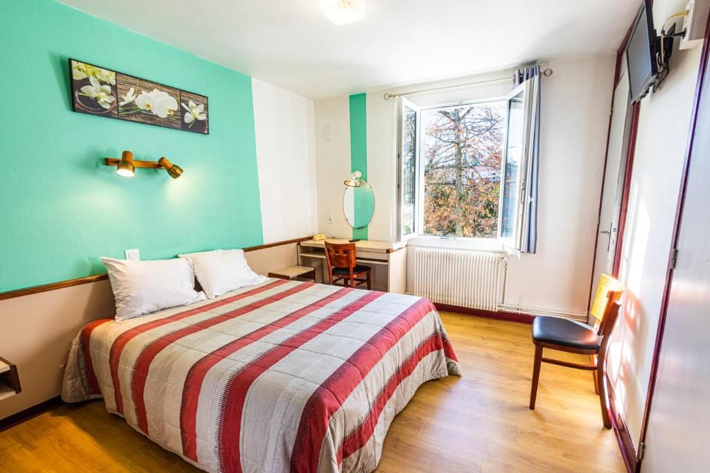 A bedroom with a bed, a desk, a chair, a window with a view, and a wall-mounted lamp.