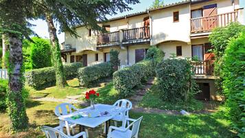 Un patio con una mesa y sillas, rodeado de vegetación y un edificio con balcones.