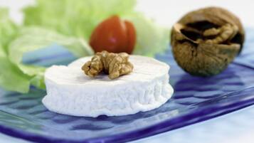 Un queso blanco redondo con nuez encima, sobre un plato azul con lechuga y una cáscara de nuez al fondo.