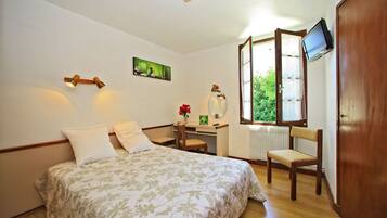 A bedroom with a bed, a desk, a chair, a TV, and a window.