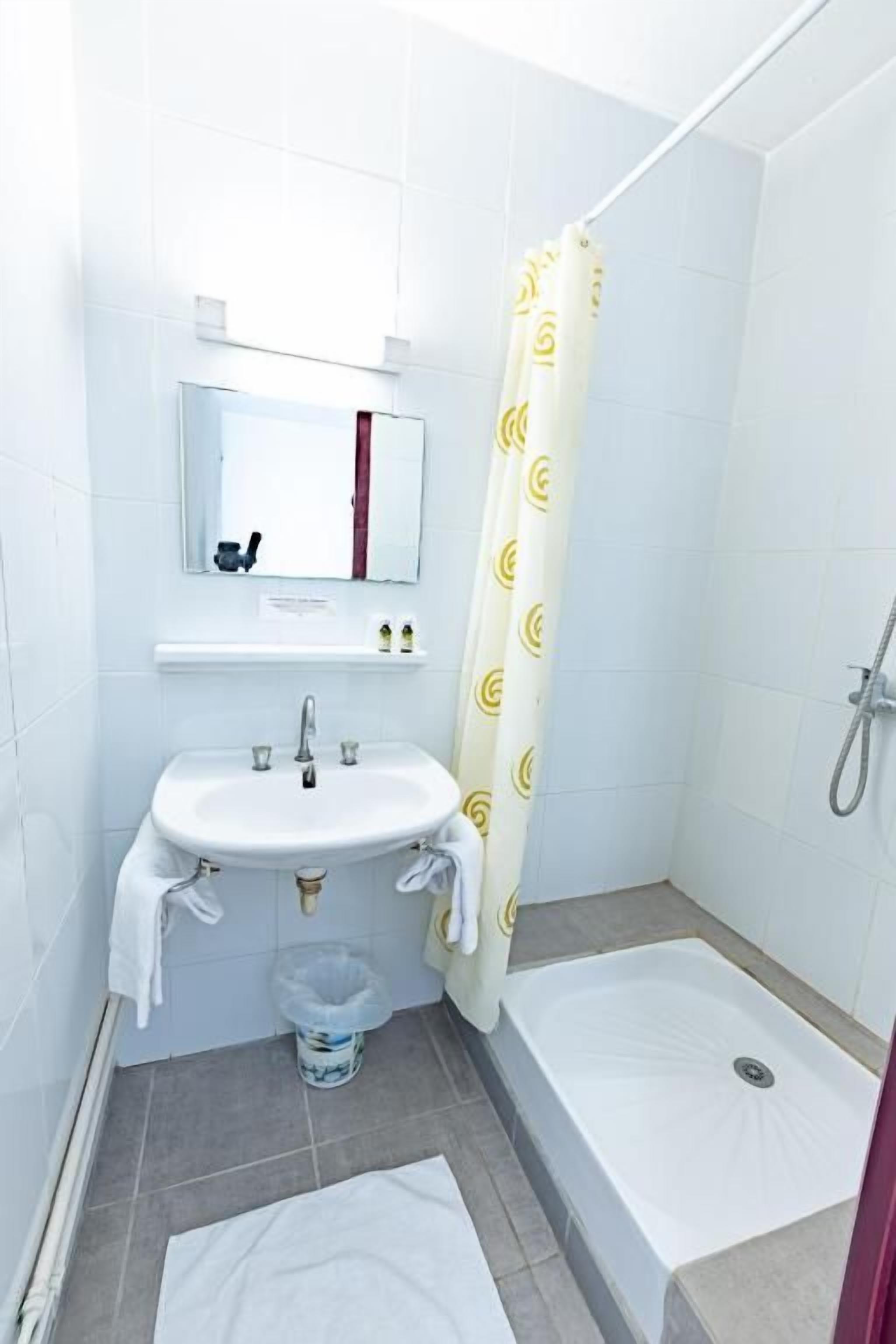 A small bathroom with a sink, mirror, shower, and a towel rack.