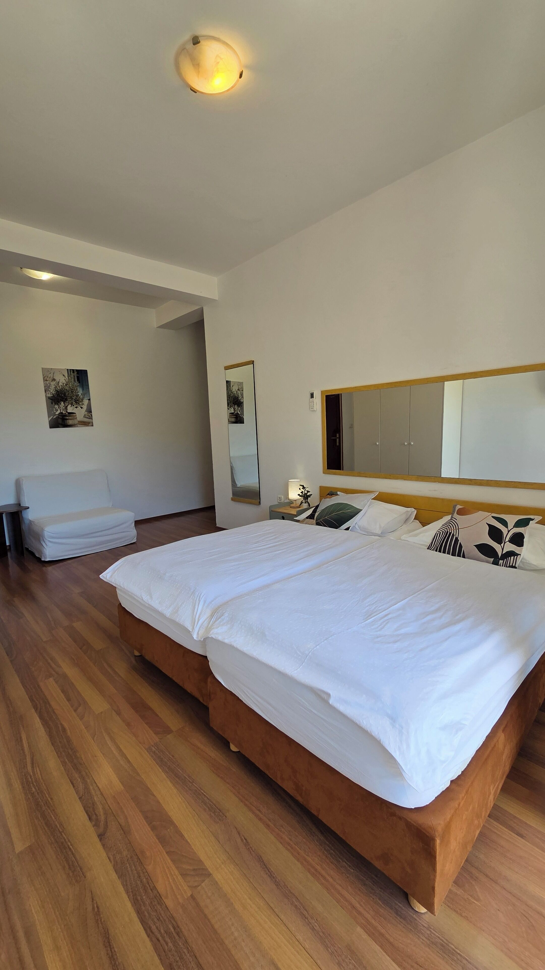 A bedroom with a large bed, a bedside table with a lamp, a mirror, and a sofa.