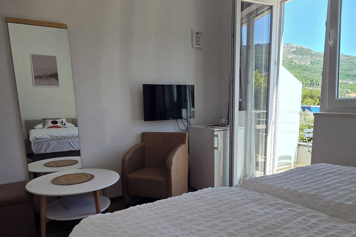 A hotel room with two beds, a TV, a chair, a small table, and a balcony with a view.