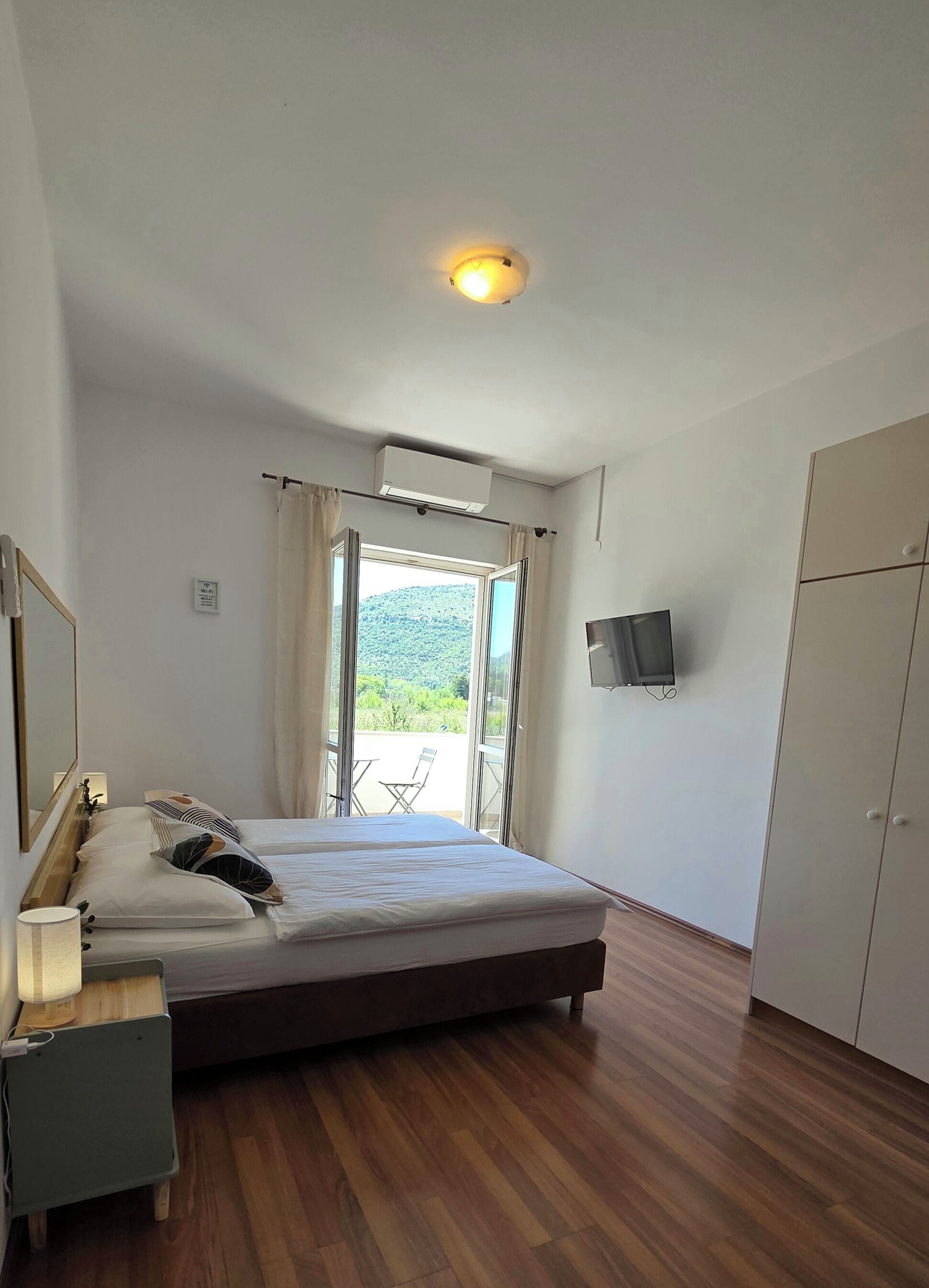 A bedroom with a bed, a bedside table, a TV, an air conditioning unit, and a wardrobe.