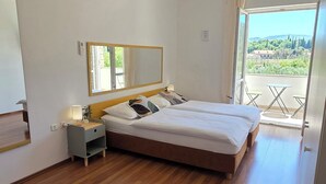 Un dormitorio con una cama grande, una mesita de noche con lámpara, un espejo y vistas al exterior a través de un ventanal.