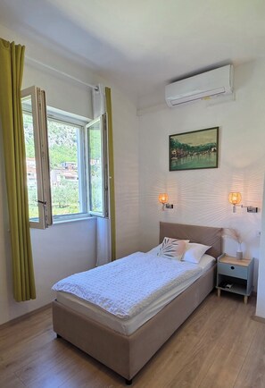 A bedroom with a bed, an air conditioner, a window with curtains, a wall-mounted picture, and bedside lamps.