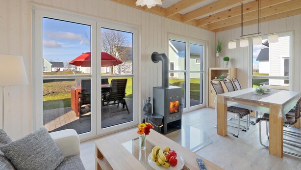 A modern kitchen with a wood-burning stove, large windows, and a dining area with outdoor seating. - Lovely home in OstseeResort Olpenitz with sauna (OstseeResort Olpenitz)