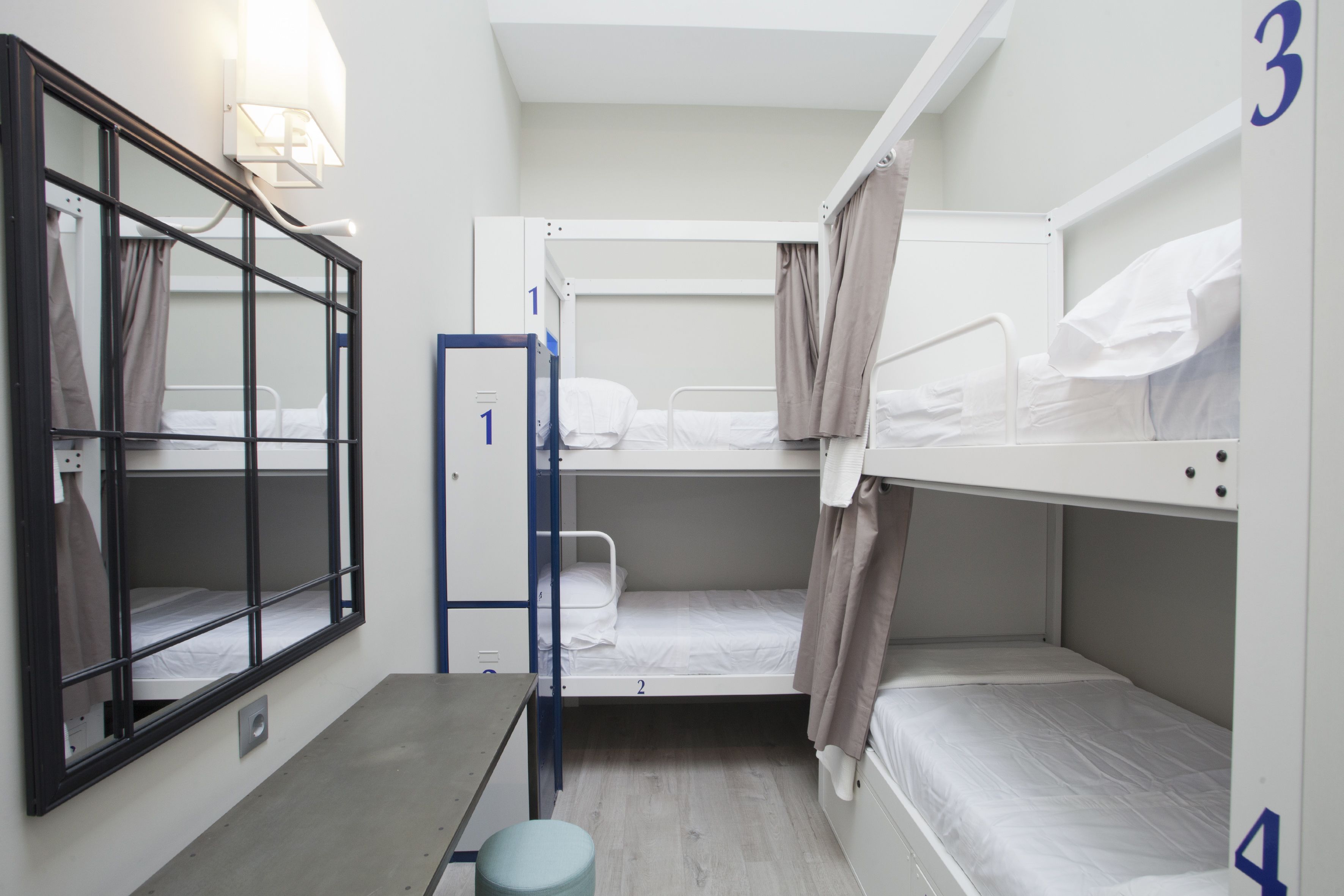 A compact hotel room with bunk beds, a small table, a chair, and a window with curtains.