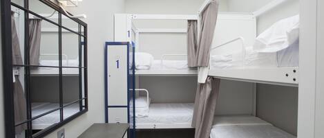 A compact hotel room with bunk beds, a small table, a chair, and a window with curtains.