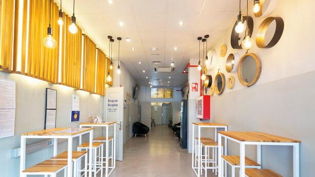 A reception area with wooden tables and benches, a reception desk, and a wall with circular mirrors. - Málaga Stop Hostel (Málaga)