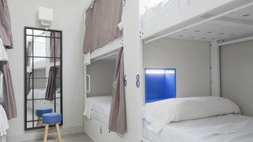 A bunk bed room with a mirror, a small stool, and a window with curtains.