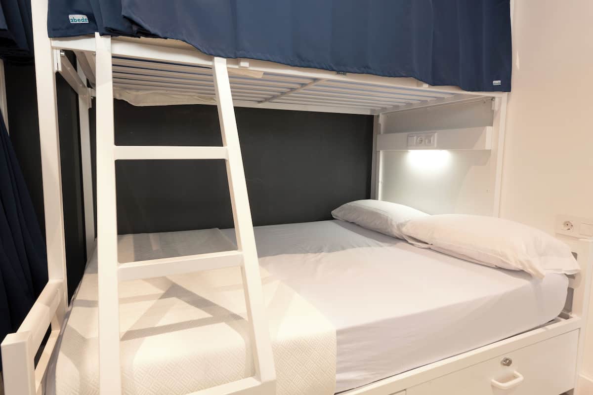 A bunk bed with a ladder, a single bed below, and a nightstand with a lamp.