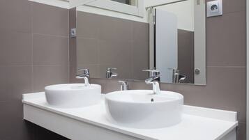 Un baño moderno con dos lavamanos blancos, un espejo grande y una lámpara empotrada en la pared.