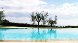 A swimming pool with a clear blue water surface, surrounded by a paved deck and a grassy area with trees. - Tenuta le Viiste (Scandicci)