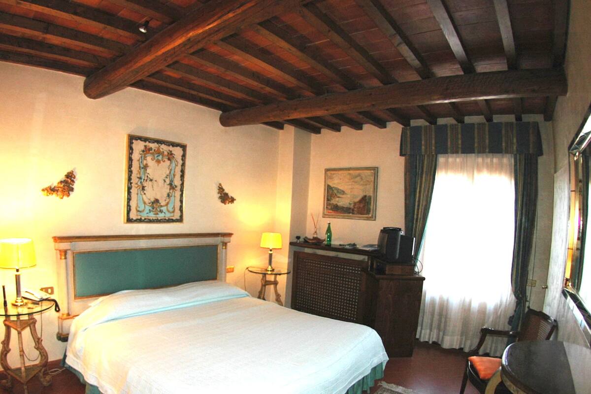 A bedroom with a large bed, a desk, a chair, a fireplace, and a window with curtains.