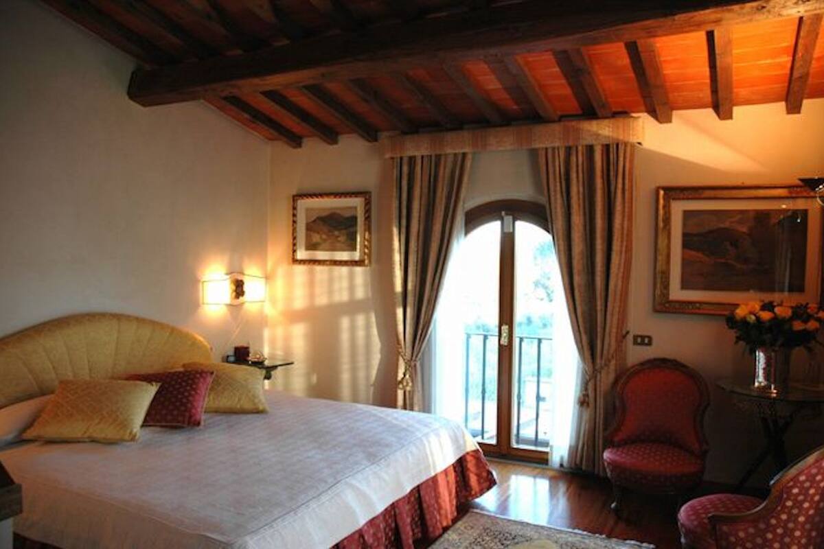 A bedroom with a large bed, a wooden ceiling, a balcony door, and a chair.