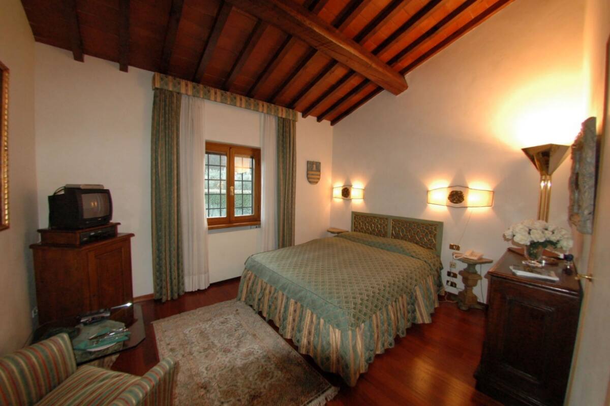 A bedroom with a wooden ceiling, a bed with a green bedspread, a television on a cabinet, and a small table with a lamp.