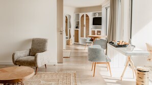 Een moderne woonkamer met een grijze fauteuil, een ronde houten salontafel en een witte dressoir met een televisie.