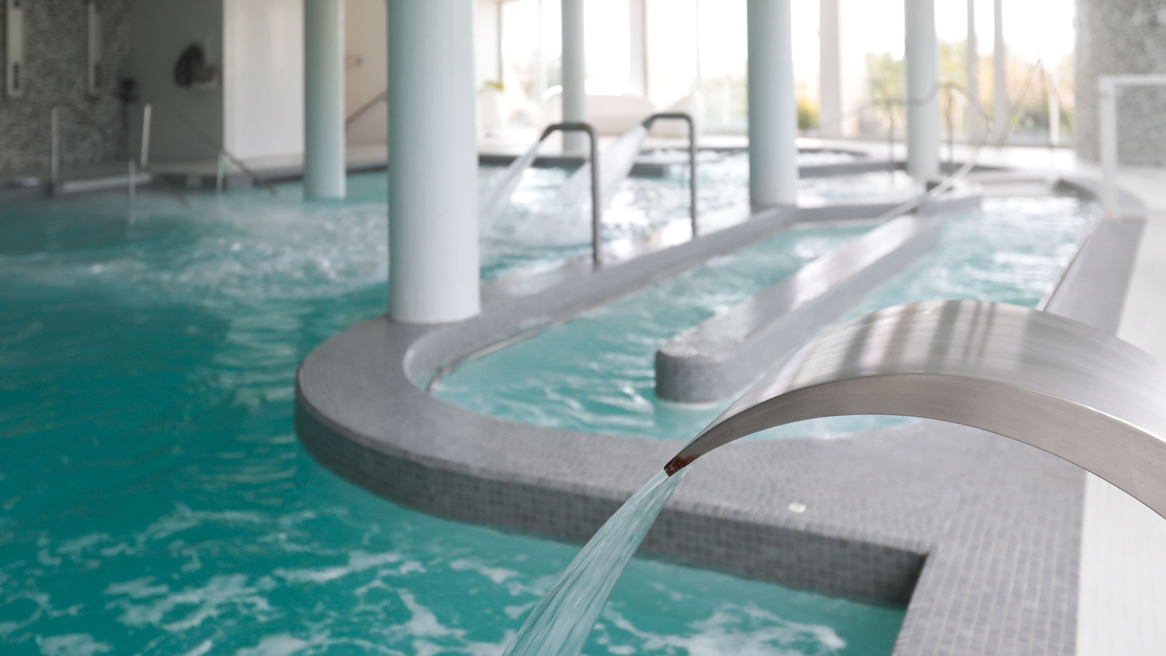 An indoor swimming pool with clear water, a curved edge, and a water feature.