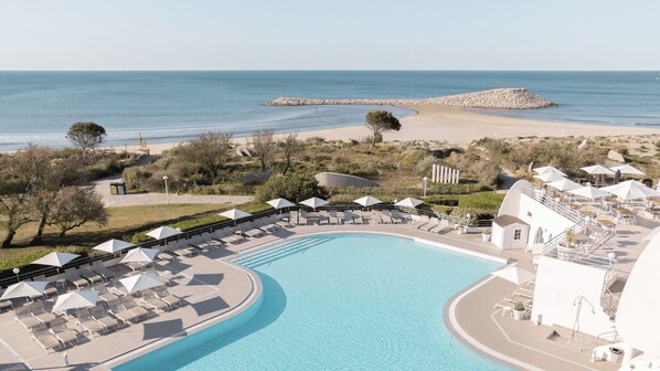 Un resort con una piscina grande, tumbonas, sombrillas y vistas a la playa y al océano.