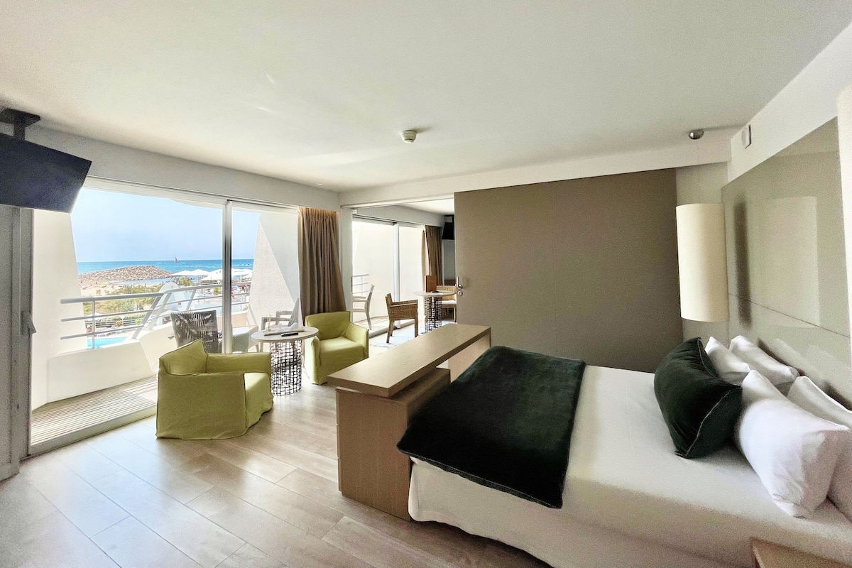 Een hotelkamer met balkon, bed, bureau en stoel.