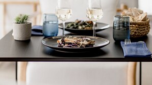 Een eettafel met borden eten, glazen witte wijn en een broodmand.
